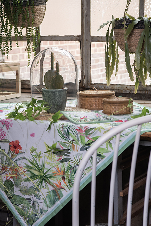 A botanical interior style with a botanical tablecloth, two wicker boxes, and a cloche with a flowerpot and a cactus in it