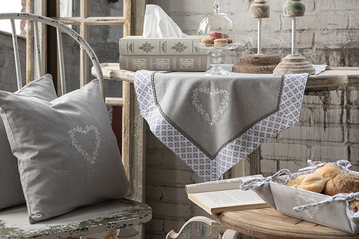 Shabby chic interior with a rural table runner embroidered with a small heart and a gray decorative cushion with an embroidered heart