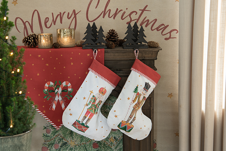 A red Christmas table runner with candy canes and two Christmas stockings hanging on a brown fireplace mantel