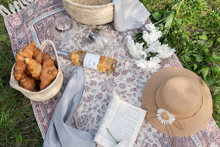 A picnic outside on a rug with two round baskets, napkins, summer hats, and wine glasses