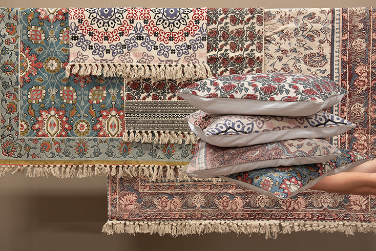 Various carpets and rugs hanging on a clothesline with four stacked decorative cushions