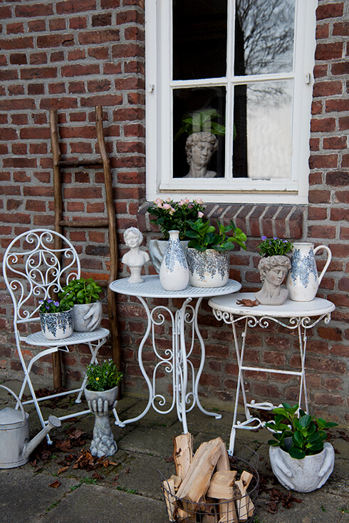 Een herfstige achtertuin met een romantische bistro tafel en bistro stoel met witte, blauwe en stenen bloempotten