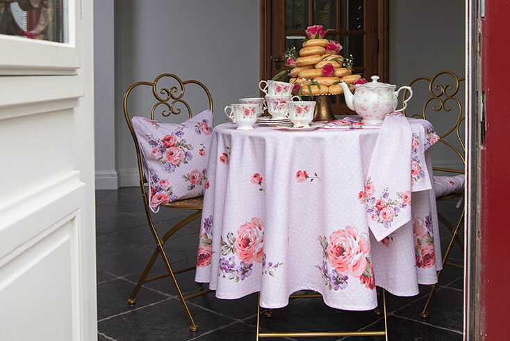 Een high tea met een goudkleurige bistro set met een roze rond tafelkleed, romantisch servies en een landelijke theepot