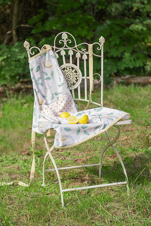A metal bistro chair with a lemon-patterned kitchen apron in the garden