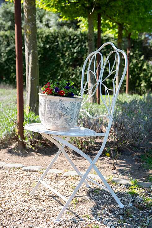 A white garden chair with a shabby chic flowerpot containing violets