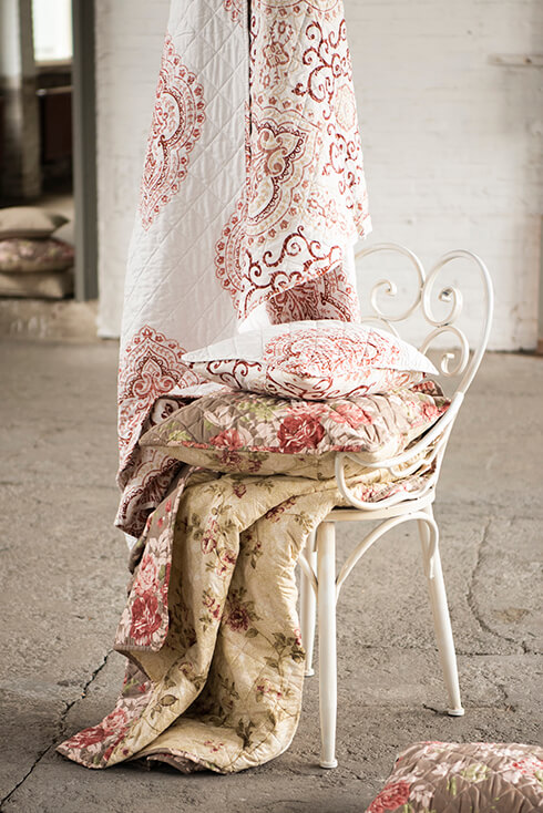 A shabby chic garden chair with stacked bedspreads and pillows