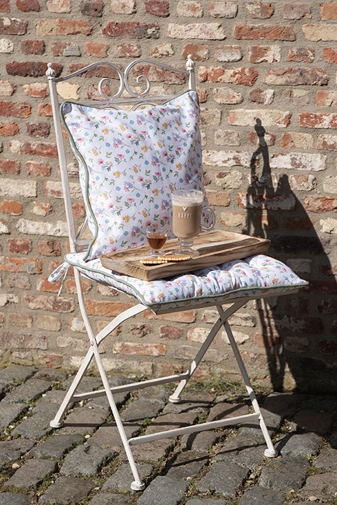 A white iron garden chair with flower-patterned garden cushions and a wooden tray with a coffee mug