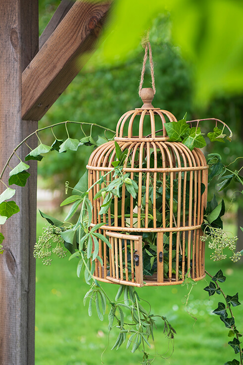 A hanging wooden birdcage with artificial greenery inside