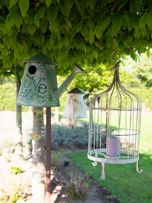 Two birdhouses hanging in the tree and a white birdcage with a candle inside, also hanging in the tree