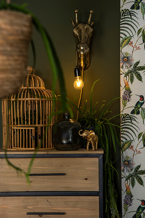 Una gabbia per uccelli in legno accanto a un vaso blu e a una statuetta di elefante dorata