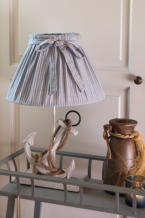 A white anchor lamp base with a fabric blue lampshade with a bow