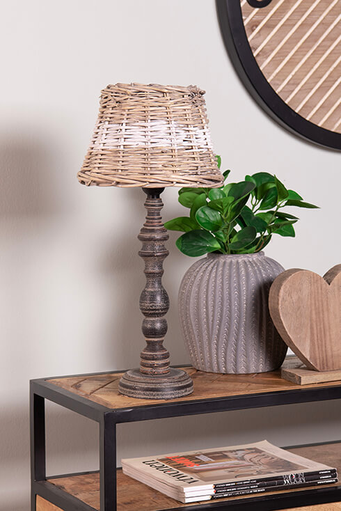 A rural black lamp base with a wicker lampshade with a white stripe and a decorative heart and a grey flower pot