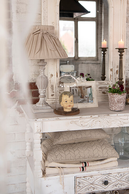 A shabby chic wall table with a rural lamp base and romantic lampshade and a dome with a figurine and a shabby chic photo frame