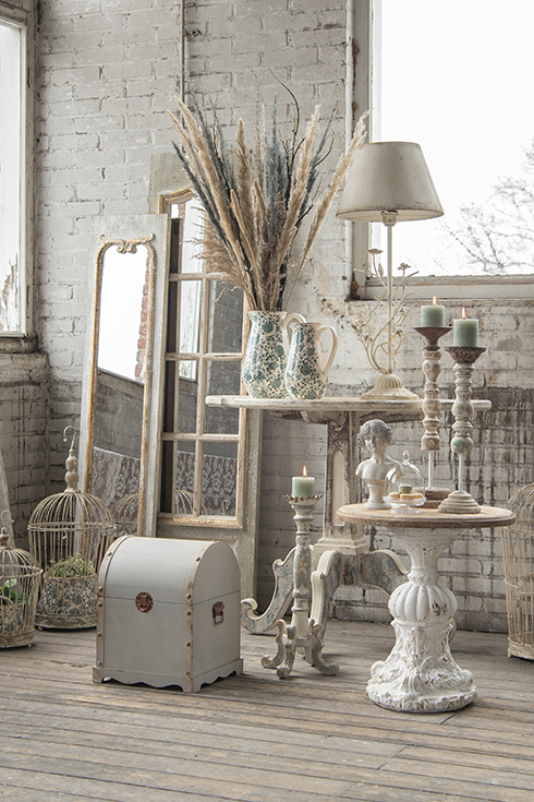 A shabby chic interior with large full-length mirrors, chests, vases, and a shabby chic table lamp