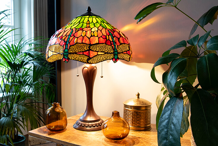 A Tiffany lamp base with a Tiffany lampshade in red and green tones with the classic dragonfly