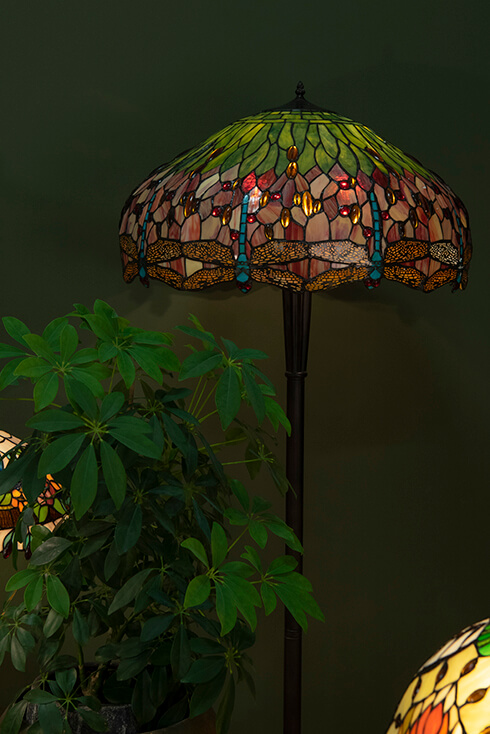 A floor lamp with a Tiffany lampshade in red and green with a blue dragonfly