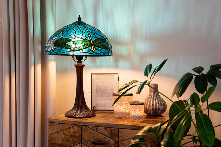 Een Tiffany tafellamp met een blauwe lampenkap met libelles en ernaast staan twee theelichthouders, een vaasje en een fotolijst