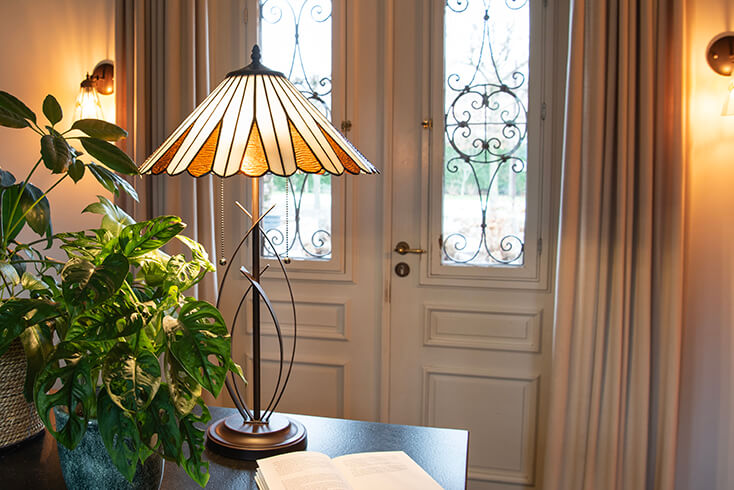 Een Tiffany tafellamp met geometrische vormen in de voet en zonnige kleuren in de lampenkap