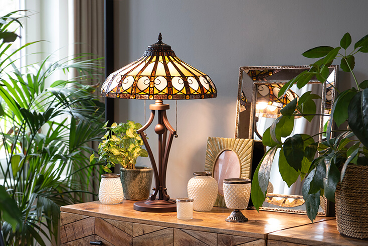 Een vintage Tiffany tafellamp in een mooie sfeer en theelichthouders, fotolijst, spiegel en een bloempotje