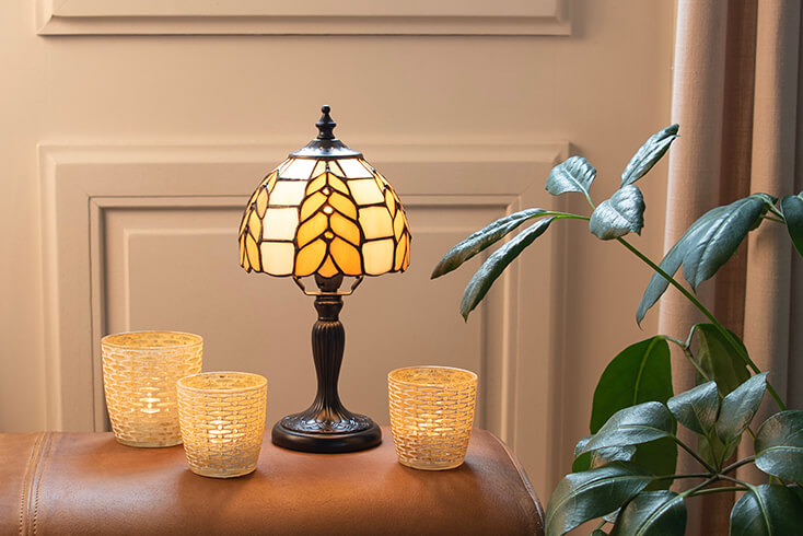 A small Tiffany table lamp on a leather footstool with three tea light holders