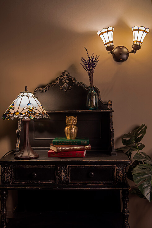 Una scrivania con una lampada da tavolo Tiffany d'epoca e una lampada da parete in vetro colorato che illumina verso l'alto con due lampadine
