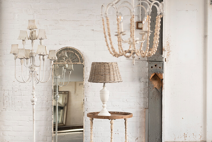 A shabby chic interior style with a rural floor lamp and a rural lamp base with a wicker lampshade, and behind it stands a shabby chic full-length mirror