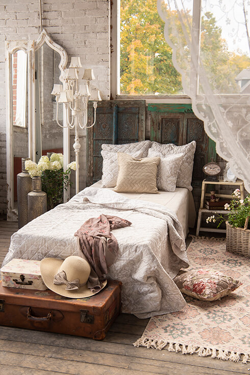 A shabby chic bedroom with a made bed and a large shabby chic floor lamp by the side