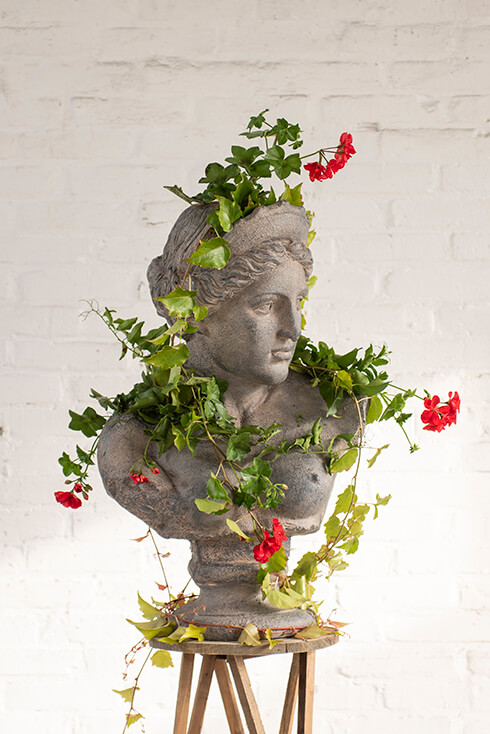 Une sculpture d'une personne entourée de fleurs sur un tabouret