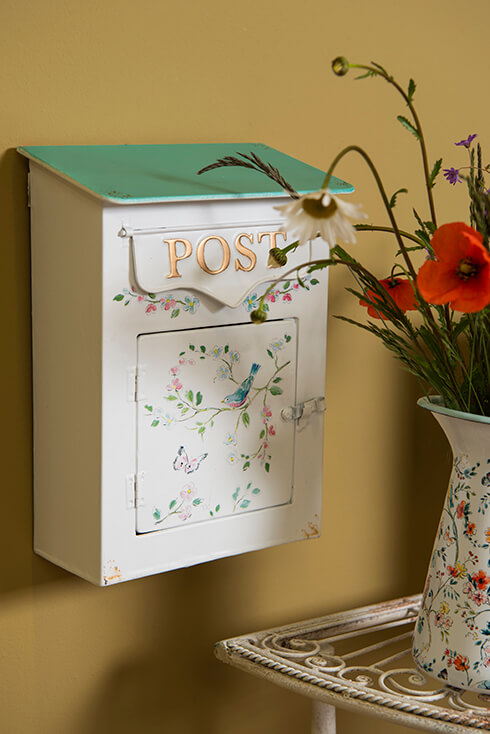Une boîte aux lettres romantique avec des fleurs, des oiseaux et des papillons, et le couvercle est vert