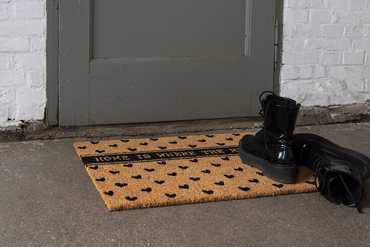 A doormat with a quote and black hearts with black boots beside it
