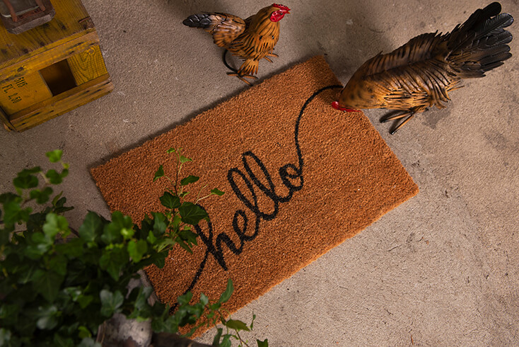 Een deurmat waar met sierletters 'hello' op staat en twee metalen kippen beelden