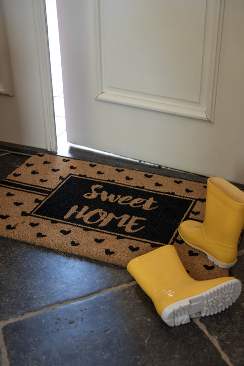 Een deurmat waar 'sweet home' op staat met gele regenlaarsjes