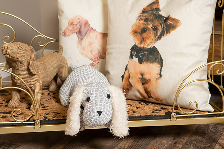 Un ferma-porta a forma di cane in un cesto per cane dorato con due cuscini decorativi con cani sopra