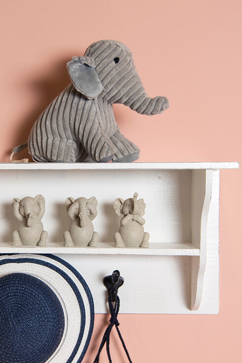 Een witte wandkast waar een olifanten deurstopper op staat en drie olifanten beeldjes van horen, zien en zwijgen