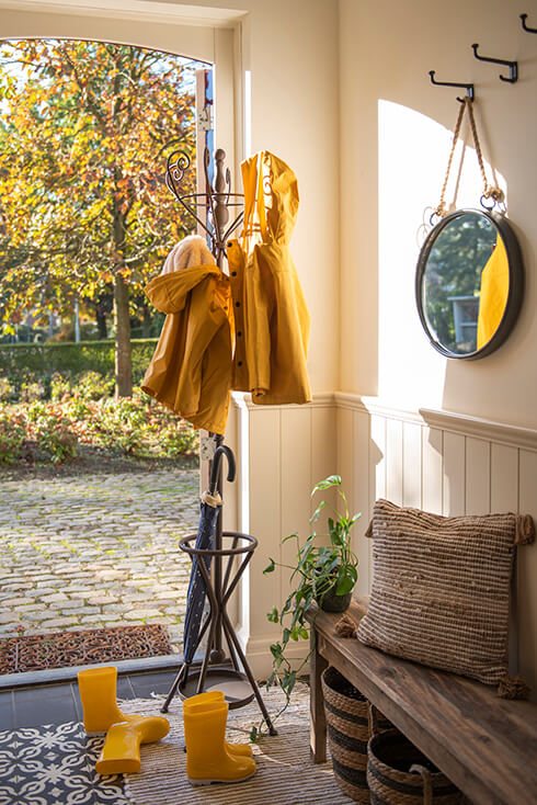 A metal standing coat rack with raincoats and an umbrella holder
