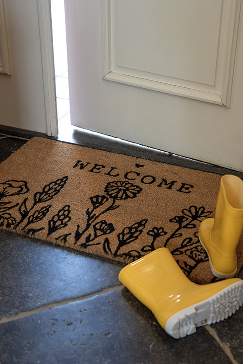 A doormat that says 'welcome' with yellow rain boots