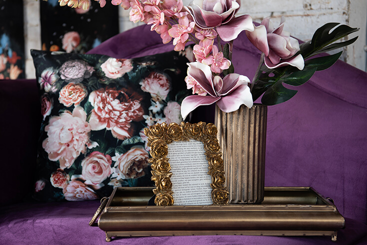 Een dienblad met een fotolijstje en een bloempot op een paarse bank