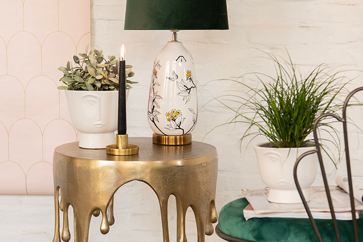 Un tavolino moderno con una lampada da tavolo moderna, un vaso per fiori bianco e un portacandele dorato con una candela nera