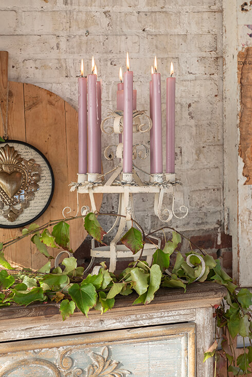 A shabby chic candle holder for multiple candles with artificial greenery around it