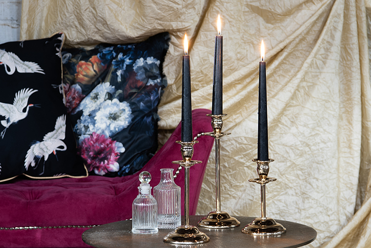 A side table with two glass bottles on it and three classic candle holders with black candles