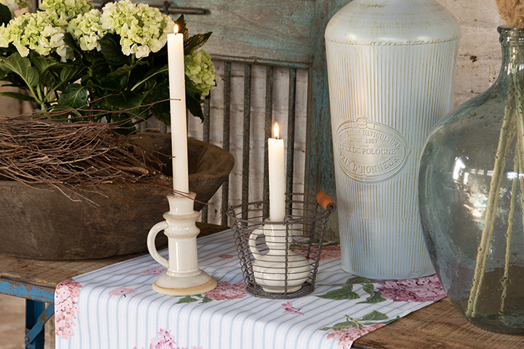 Two ceramic candle holders with a black basket on a hydrangea table runner