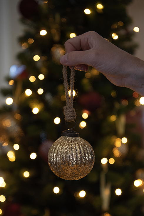 A golden Christmas ornament with a Christmas tree in the background