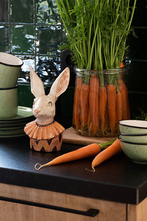 Een aanrecht met borden, kommen een pot met wortelen en een beeldje van een konijn