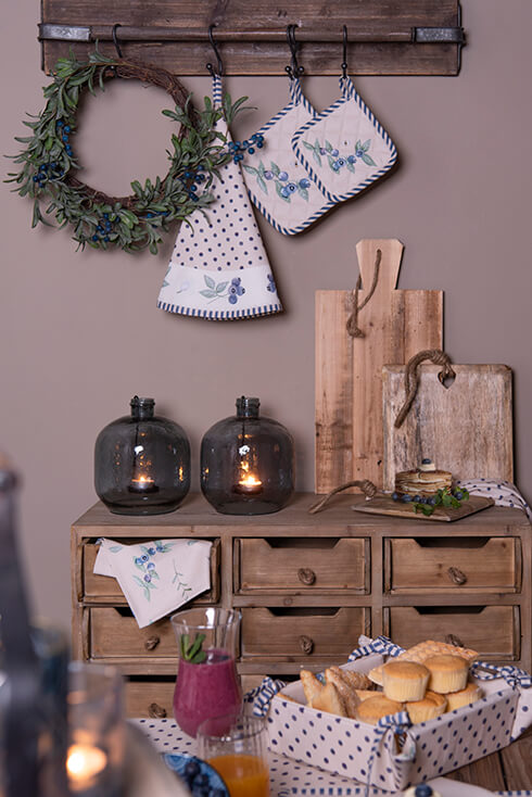 A set table, a cabinet with candles and breadboards, and above it a coat rack with a wreath hanging on it