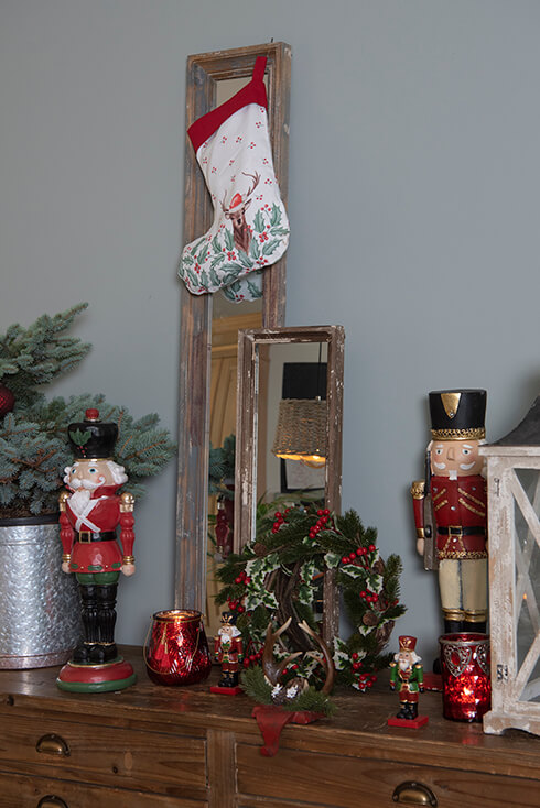 A cabinet with candle holders, mirrors, a Christmas stocking, and a wreath