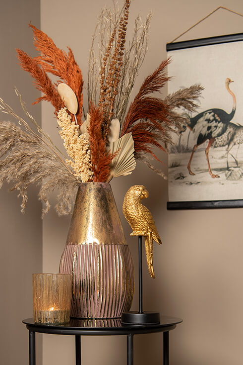 Een gouden beeldje van een vogel, een bloempot met kunstplanten en droogbloemen op een bijzettafel