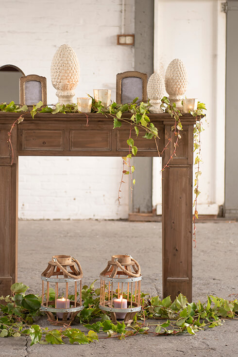 Una mensola marrone con piante artificiali e decorazioni per la casa, sotto cui ci sono due lanterne di legno