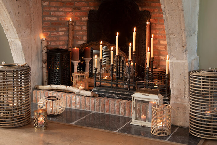 Une cheminée remplie de porte-bougies rustiques, comprenant un grand chandelier, des lanternes et plus encore