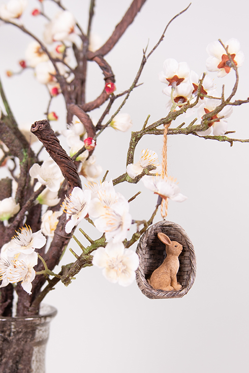 Un petit lapin assis en tant que suspendu de Pâques à une branche