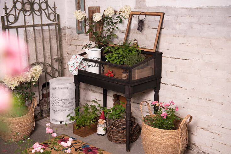 A garden with baskets, flowers, plants, and in the corner a white trash can